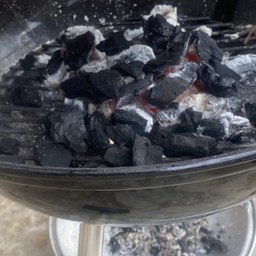 Brasas de carbón vegetal encendidas con ceniza blanca en una barbacoa Weber
